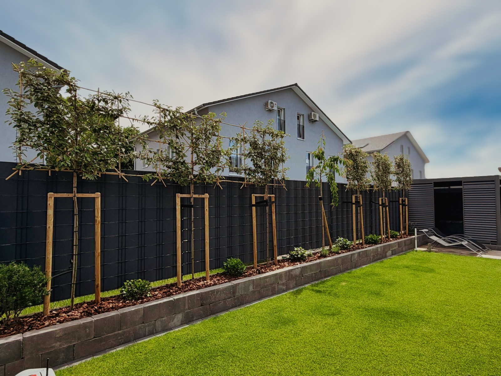 Neu angelegte Gartenanlage mit Rollrasen, Hochbeet, Sichtschutzzaun und gepflanzten Bäumen.